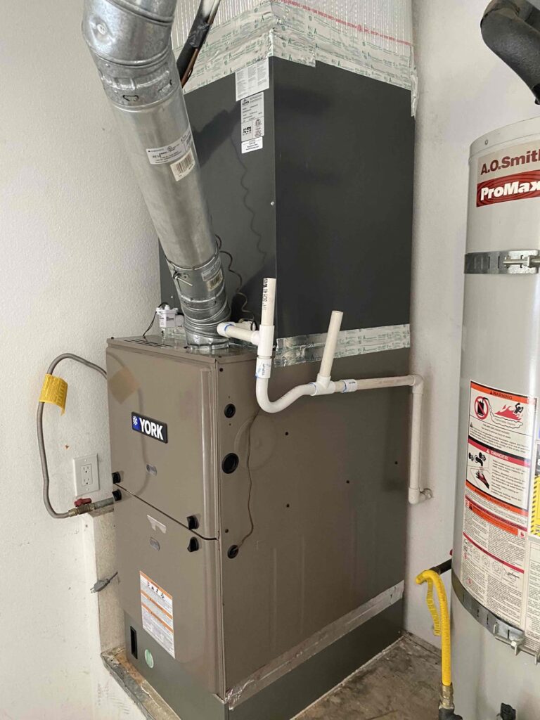 A York HVAC furnace unit with attached ductwork and PVC pipes is installed indoors next to a hot water heater tank.