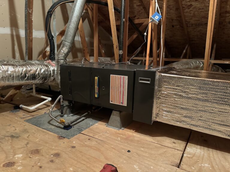 An HVAC air handler unit is installed in an attic with exposed wooden beams and ductwork connected on both sides.