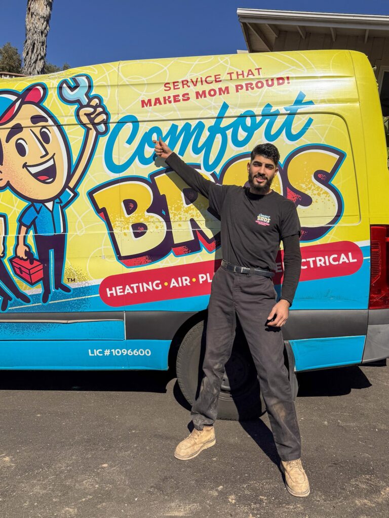 A man in work clothes stands in front of a Comfort Bros service van, pointing at the slogan “Service That Makes Mom Proud!” printed on the side.