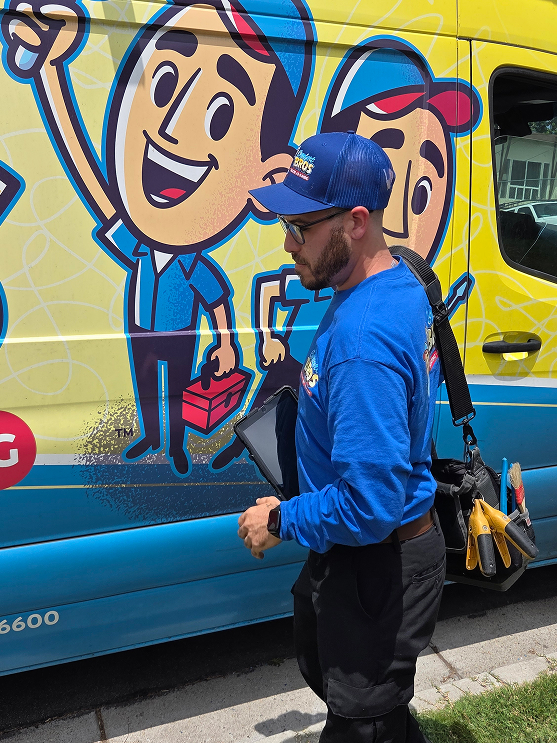 A technician in a blue uniform stands next to a van with a cartoon graphic of workers, holding tools and a tablet.