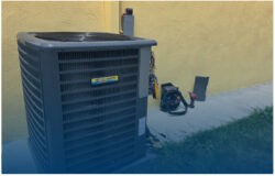 A central air conditioning unit sits outside a yellow building with tools and equipment placed nearby on the concrete.