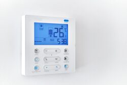 A digital wall-mounted thermostat displays a temperature of 26°C and the time 5:38, with various control buttons and icons visible on the screen.