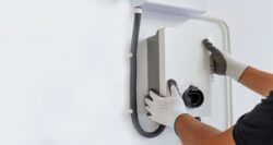 Person wearing gloves installs or adjusts an electric vehicle charging station mounted on a white wall.