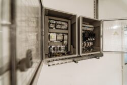 Two open electrical control panels with switches, relays, and wiring mounted on a wall inside a building.