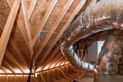 Exposed HVAC ductwork and wooden beams in a residential attic with unfinished walls and ceiling.
