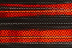 Close-up of a red electric heater with glowing heating elements, viewed through a black safety mesh or grill.